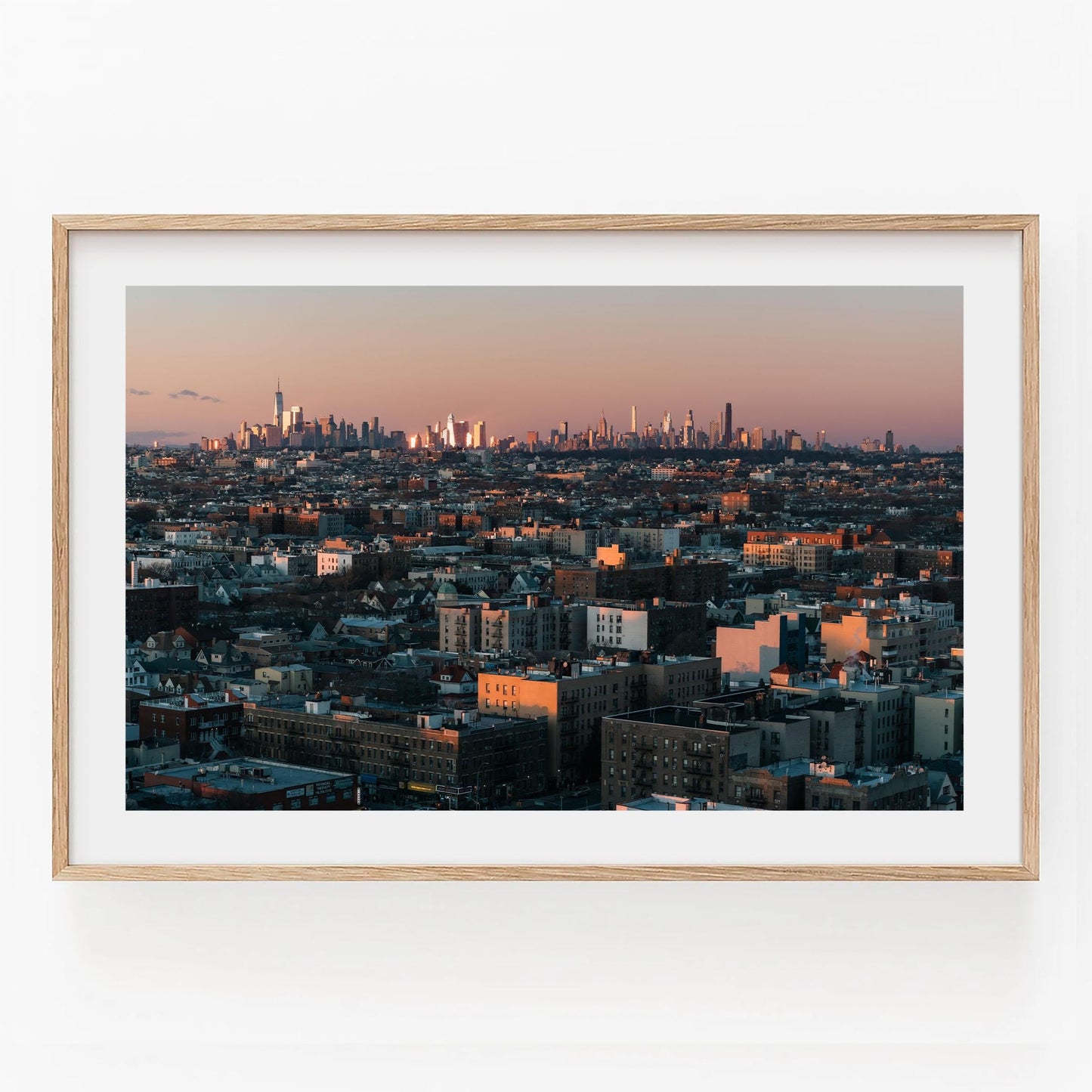 Skyline From Brooklyn: A framed photo of a sunset cityscape with glowing skyscrapers beneath a pink and orange sky.