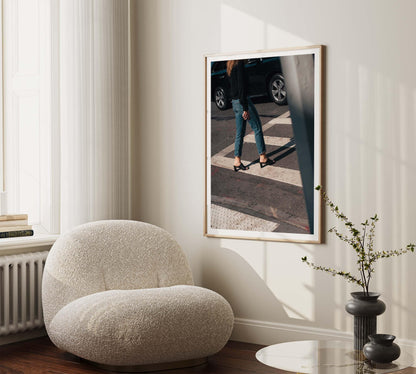 A cozy room with Sunday Chic—a plush chair, small table with vases, and framed photo of a person crossing a street.