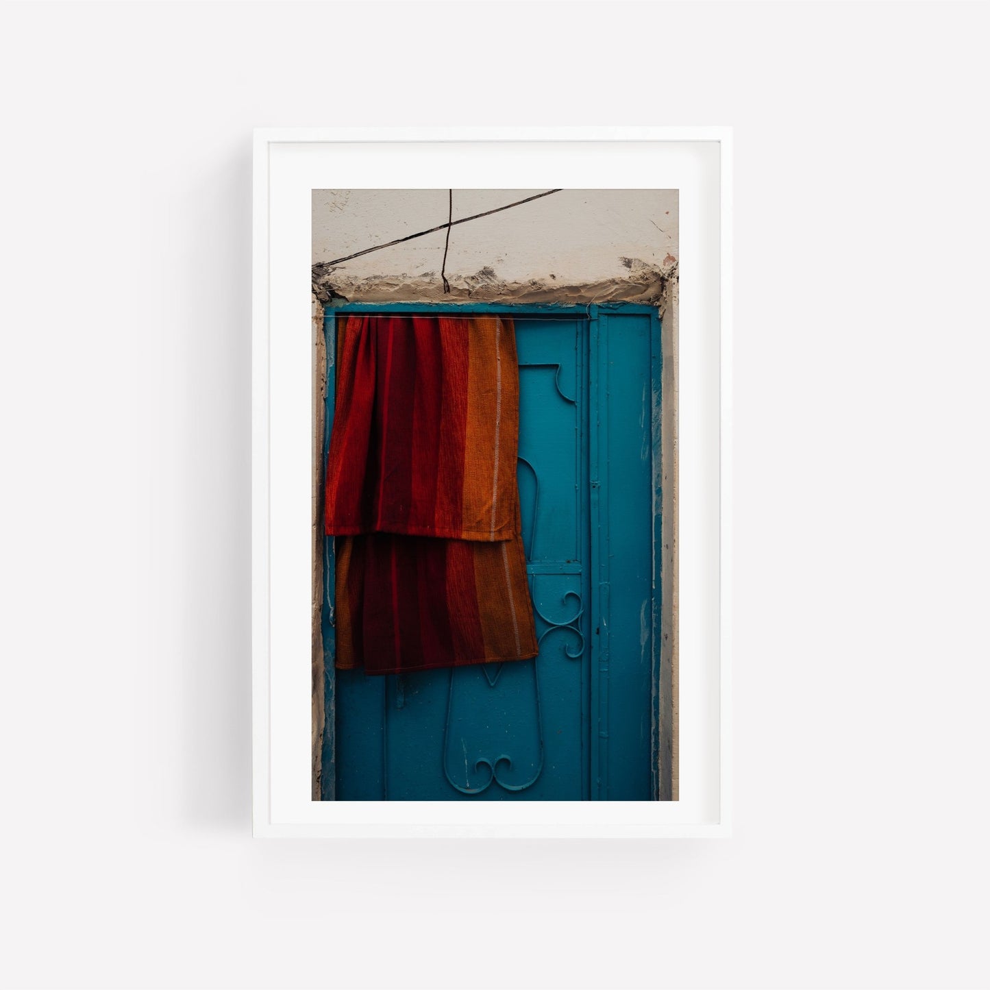 Framed Taghazout Door photo featuring a blue ornate door with red and orange fabric draped over it.
