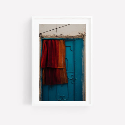 Framed Taghazout Door photo featuring a blue ornate door with red and orange fabric draped over it.