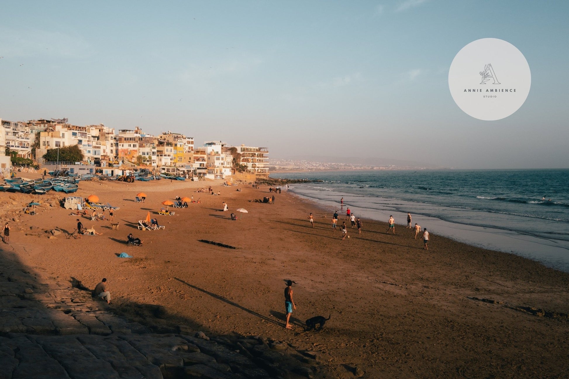 People enjoy a sunny day on Taghazout I beach in a coastal town with gentle waves in the background.