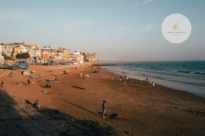 People enjoy a sunny day on Taghazout I beach in a coastal town with gentle waves in the background.