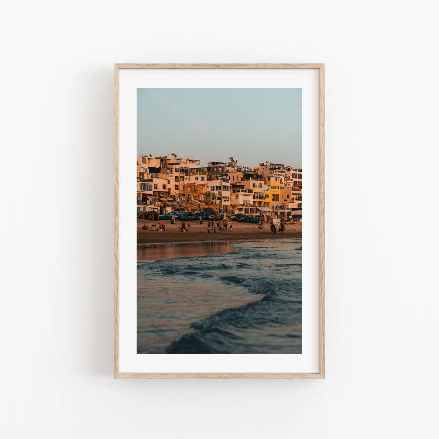 Framed Taghazout Wave photo of a coastal town at sunset with beachgoers and waves in the foreground.