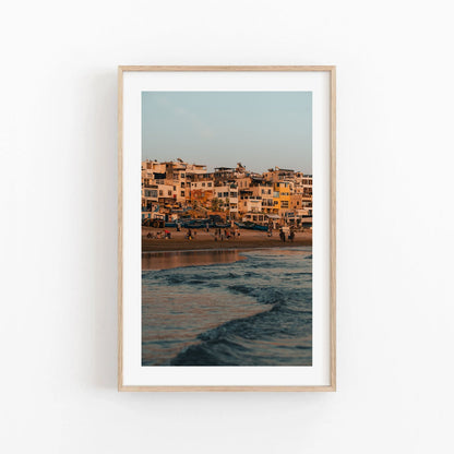 Framed Taghazout Wave photo of a coastal town at sunset with beachgoers and waves in the foreground.