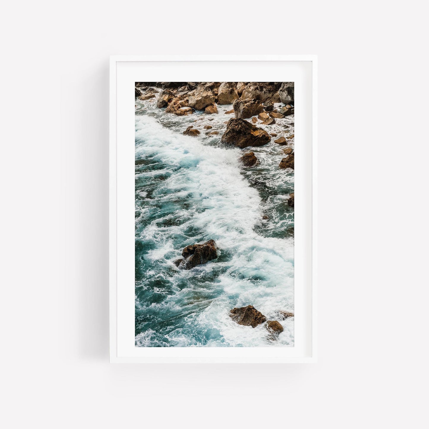 Teal Tide: A framed photo of ocean waves crashing on rocks, displayed on a white wall.