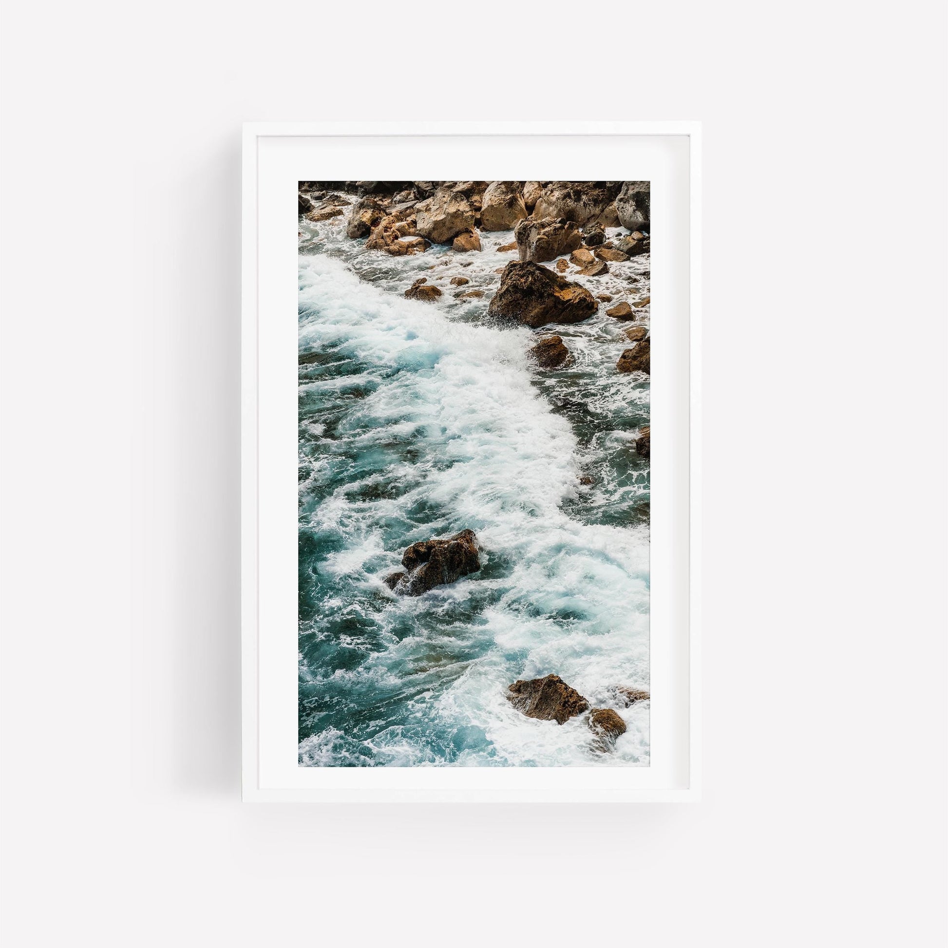 Teal Tide: A framed photo of ocean waves crashing on rocks, displayed on a white wall.