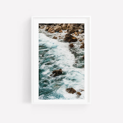 Teal Tide: A framed photo of ocean waves crashing on rocks, displayed on a white wall.