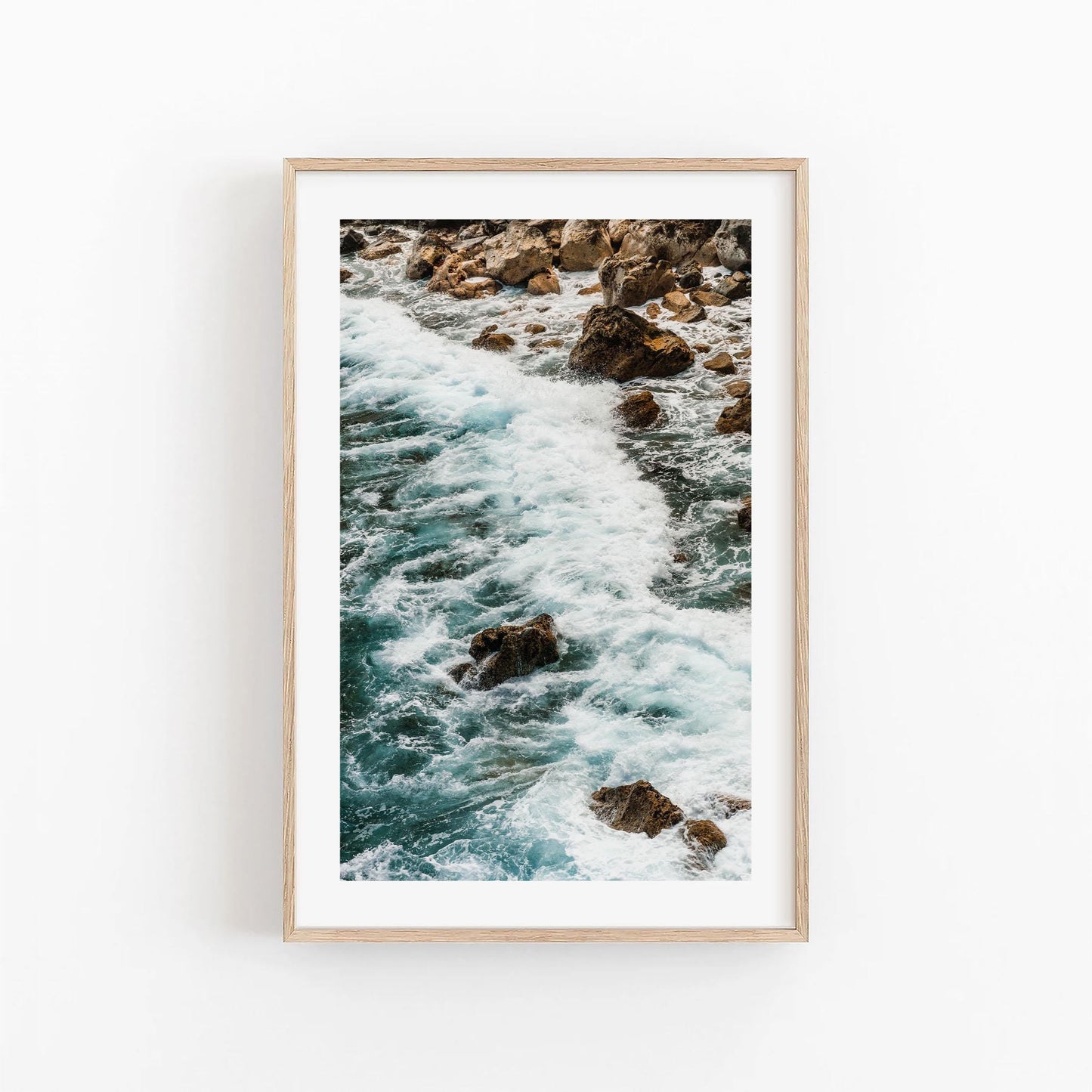 Teal Tide framed photo of ocean waves on rocks, showcased on a white wall.