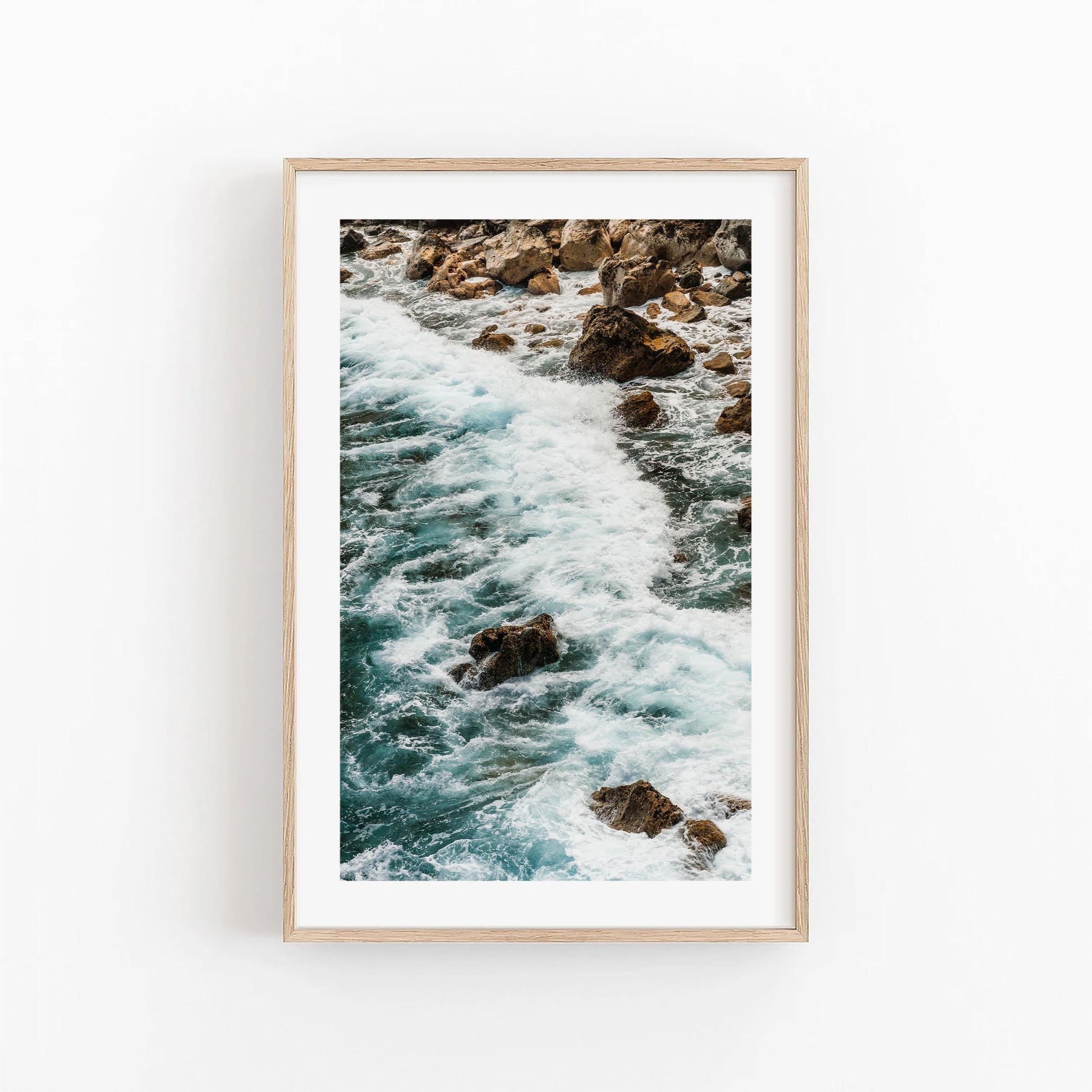 Teal Tide framed photo of ocean waves on rocks, showcased on a white wall.
