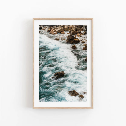 Teal Tide framed photo of ocean waves on rocks, showcased on a white wall.