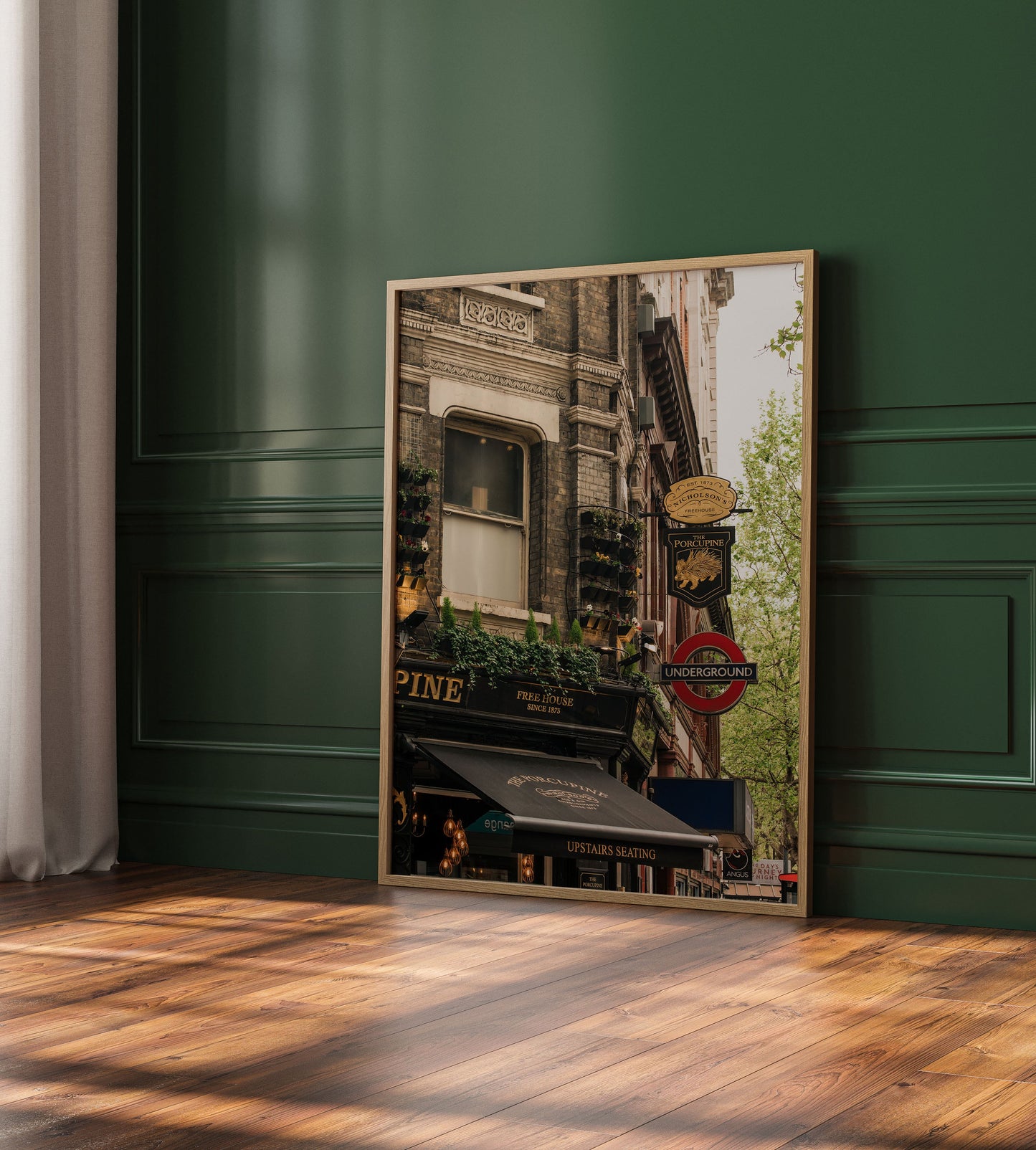 A framed print of "The Porcupine Pub" leans against a green wall on a wooden floor in sunlight.