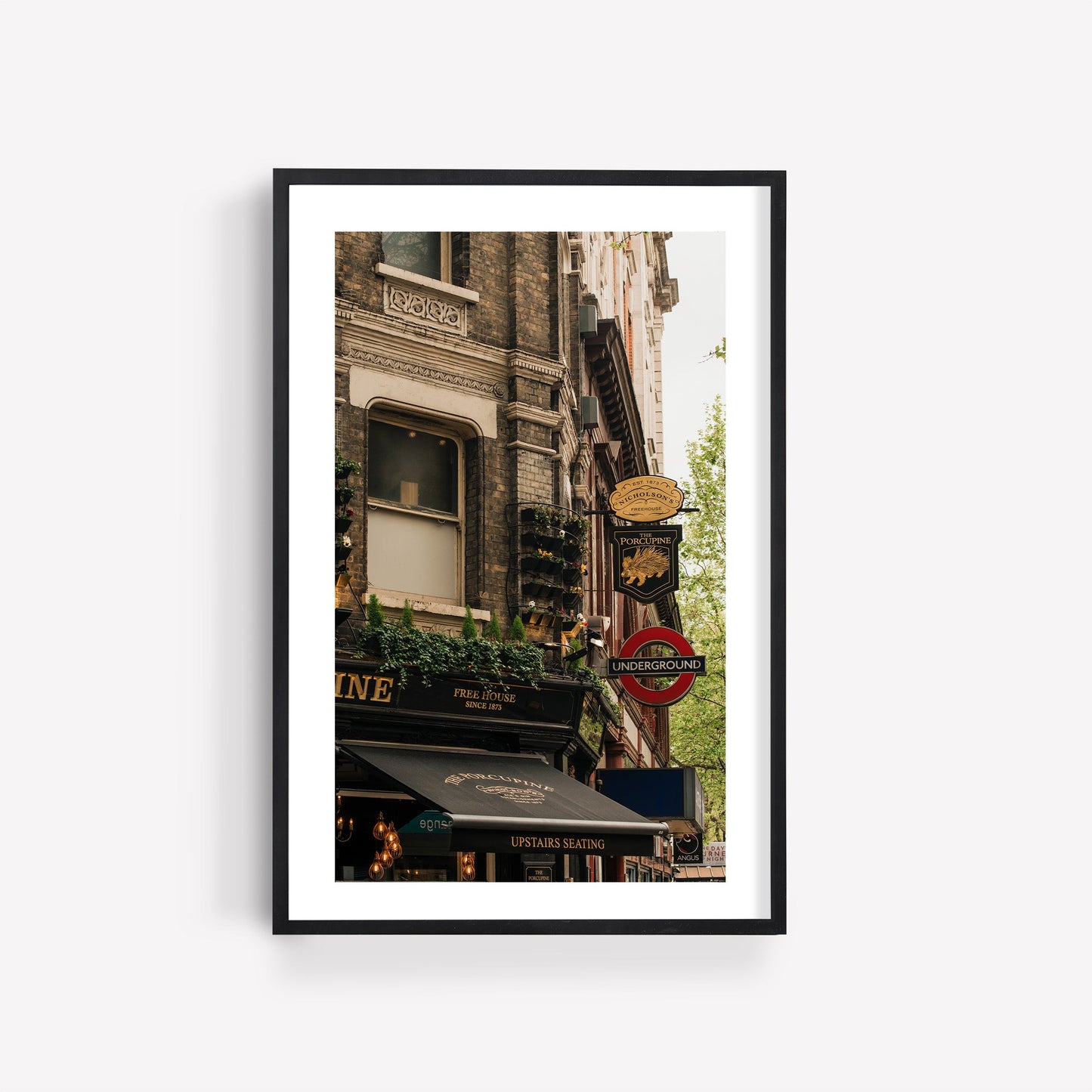 Framed photo of The Porcupine Pub with restaurant signs and a London Underground sign on a city street.