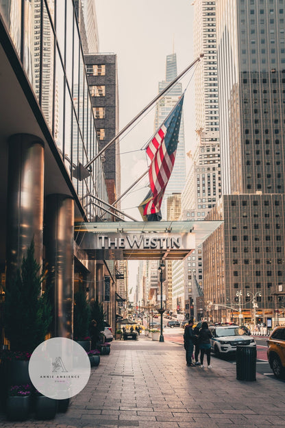 City street view with tall buildings, a big American flag, and The Westin sign as people stroll on the sidewalk.