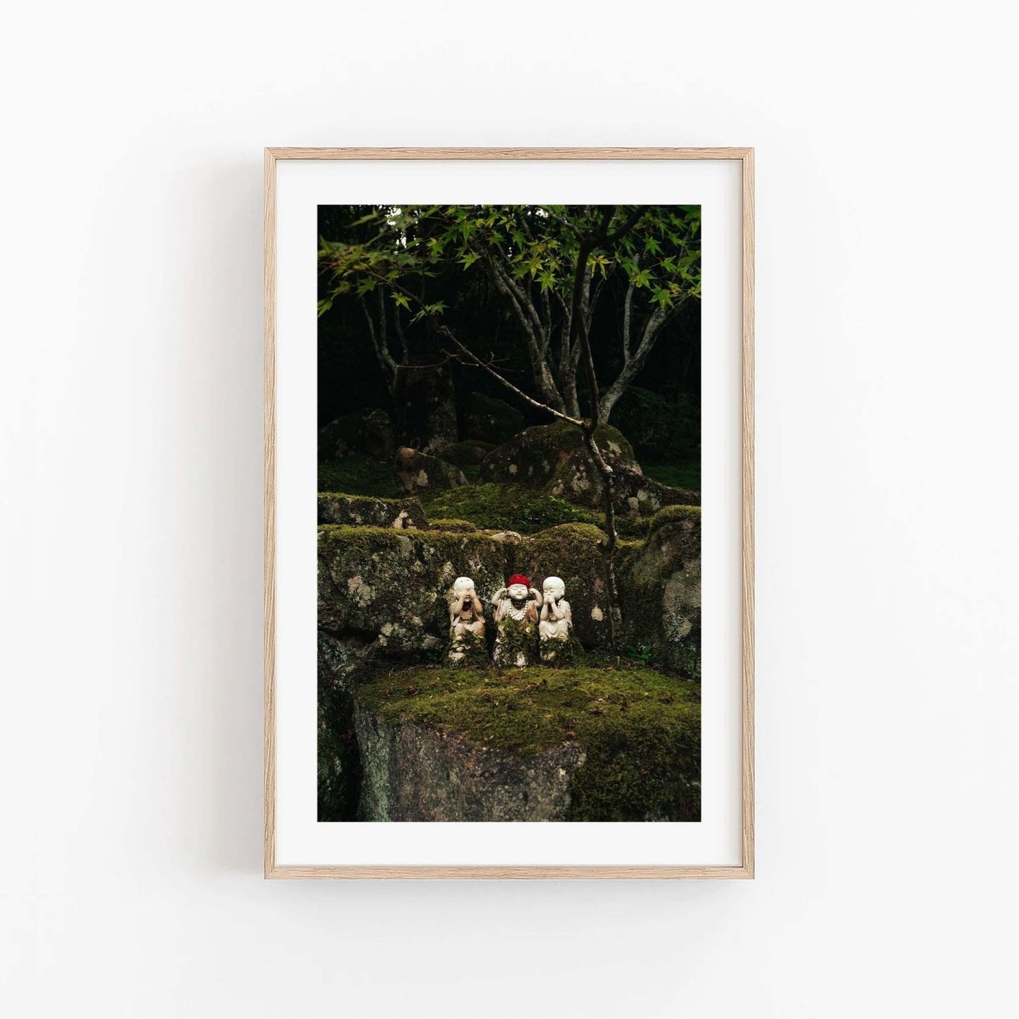 Wall art titled Three Wise Ones showcasing three small stone statues on a moss-covered rock with trees in the background.