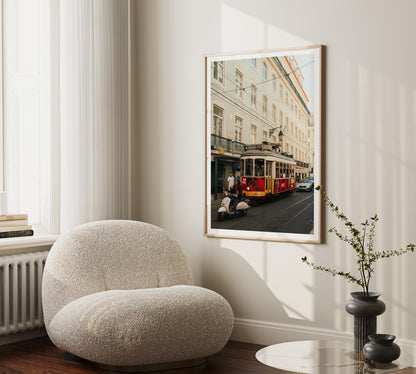 A cozy chair and vase beside a Tram 28 photo of a red tram, hung on a light-colored wall.