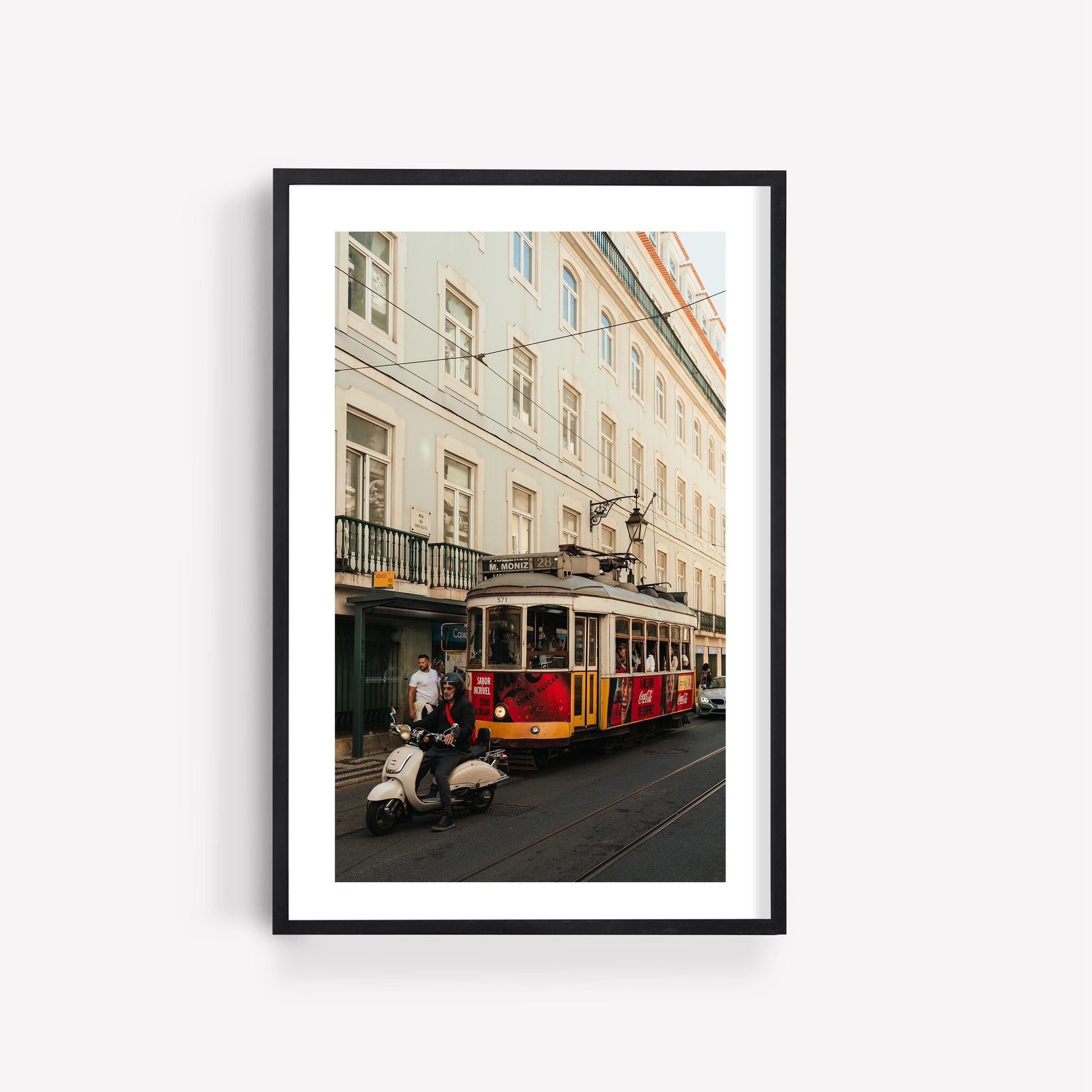 Framed photo, Tram 28: Yellow tram and scooter rider in front of pastel city buildings.