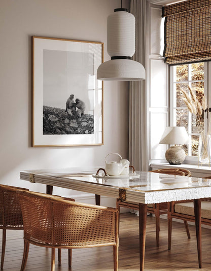 Dining room with large table, wicker chairs, framed Two Monkeys Black and White art, and a window view with natural light.