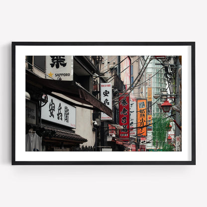 Urban Tapestry framed photo captures a lively Japanese street scene with vibrant signs and power lines.