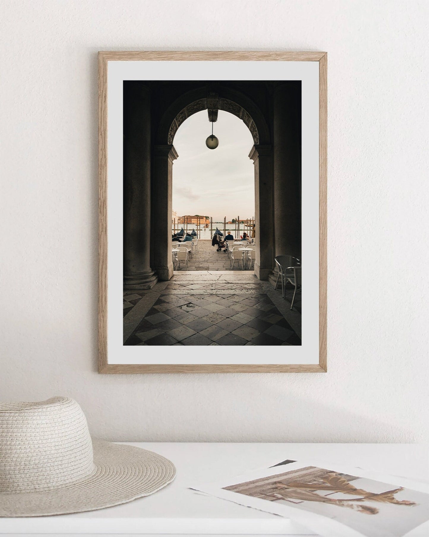 The Venice Arch framed photo hangs above a table with a hat and papers, showcasing an archway with a distant city view.