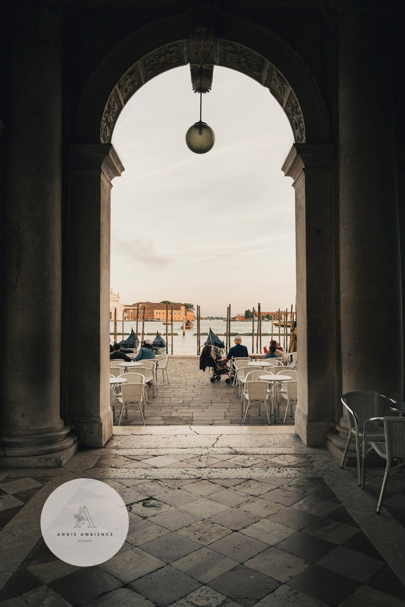 View through Venice Arch of an outdoor café with boats and an island under a cloudy sky.