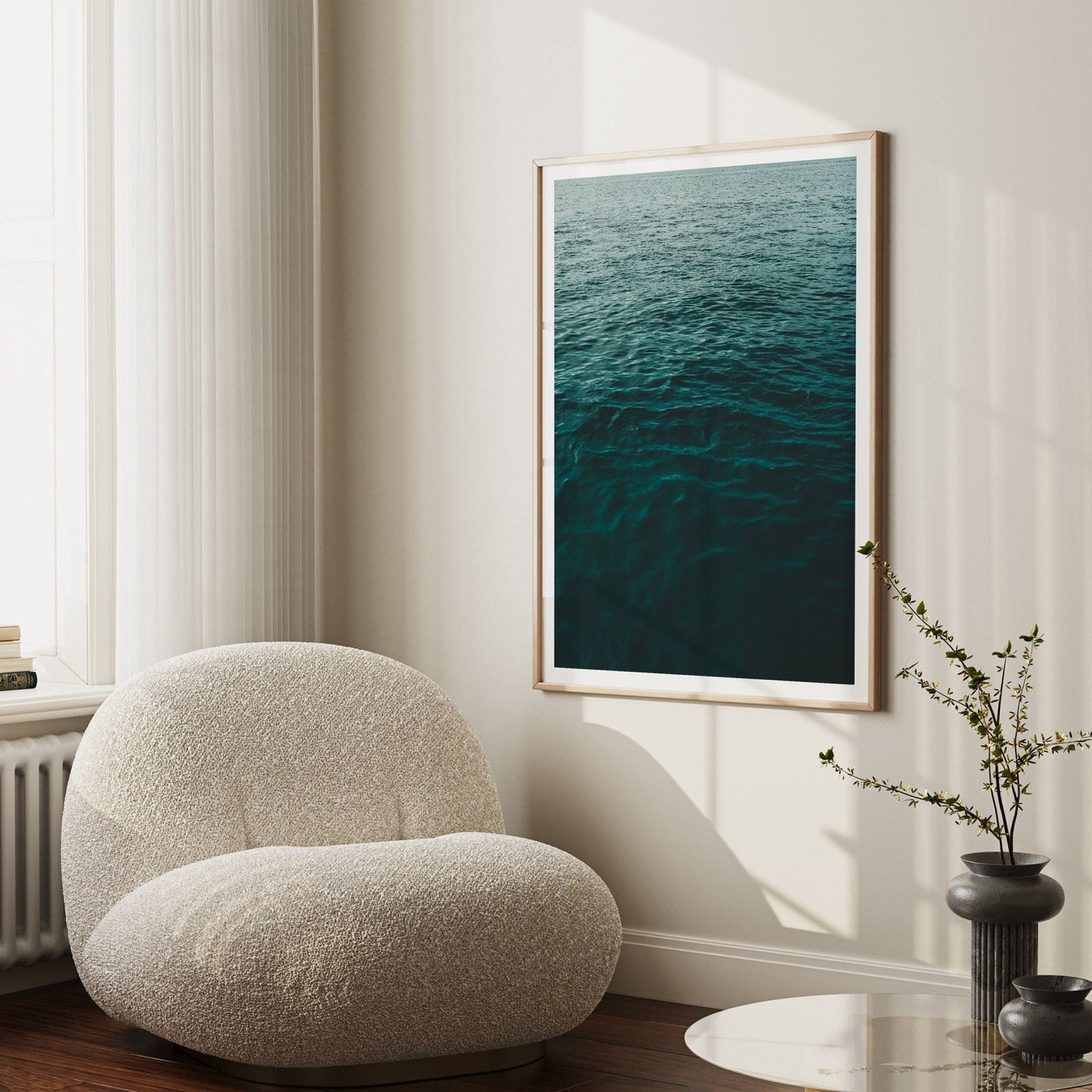 A cozy beige chair in a sunlit room with Water Ripples II on the wall and a small plant on a round table.