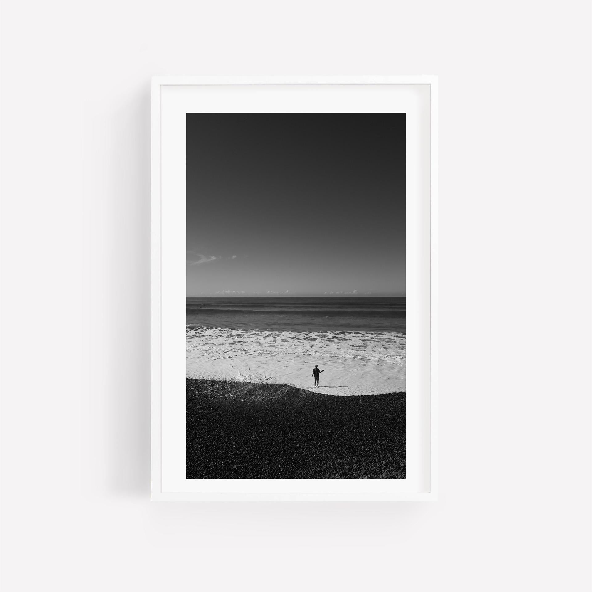 Waves at Your Feet Black and White photograph of person on pebble beach, framed with a white mat and frame.