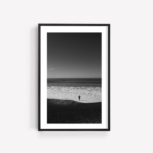 Product Waves at Your Feet Black and White framed on a white wall, shows a person facing the ocean.