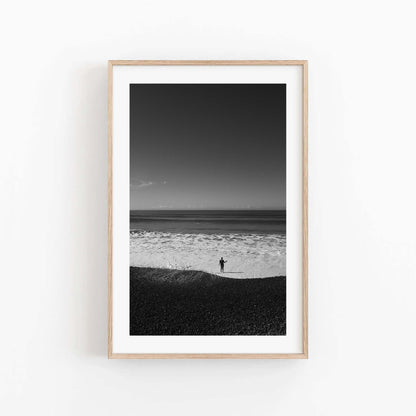 Waves at Your Feet Black and White: Framed photo of a person standing alone on a beach, facing the ocean under a clear sky.