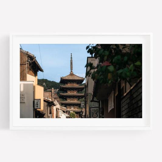 The Yasaka Splendor is a framed photo capturing a pagoda view through a narrow street lined with traditional buildings and greenery.