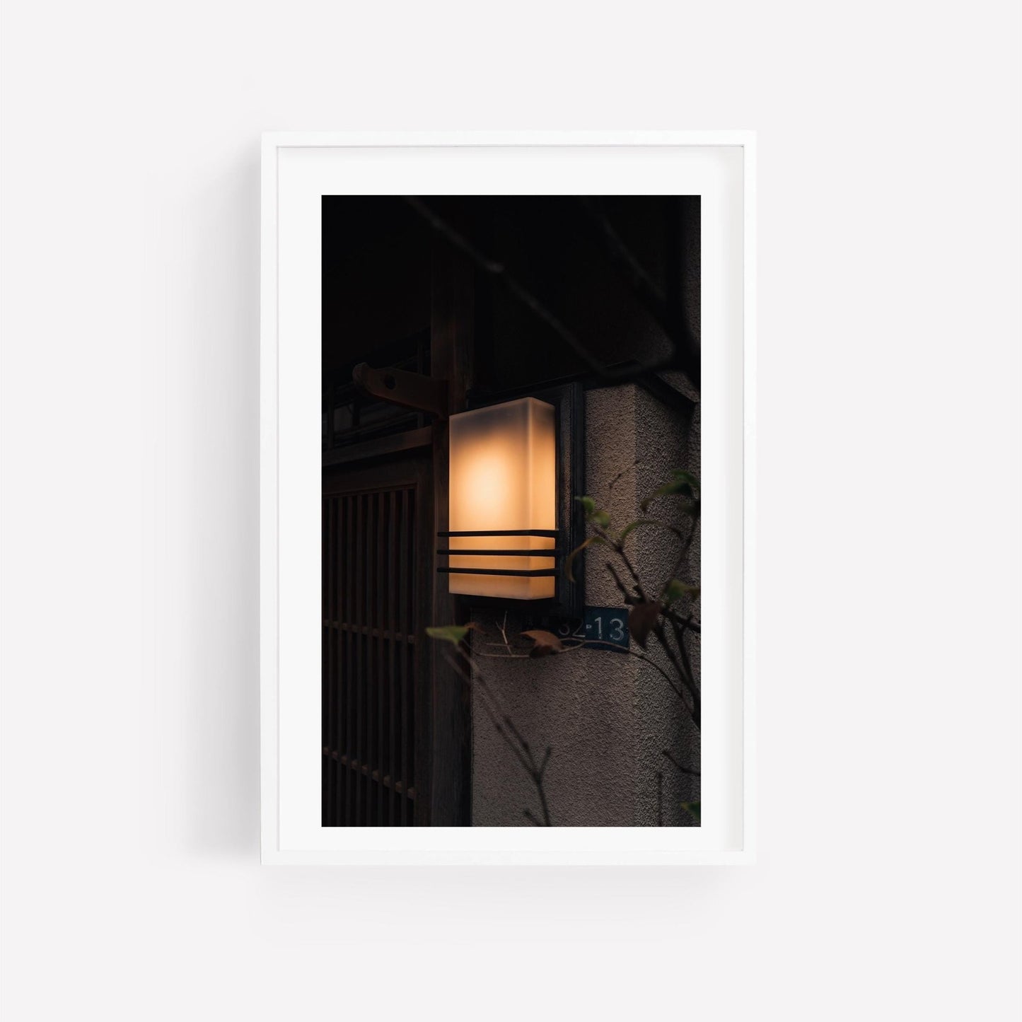 The Zen Ambience wall-mounted lantern bathes a homes exterior in a warm glow, partially concealed by leaves.