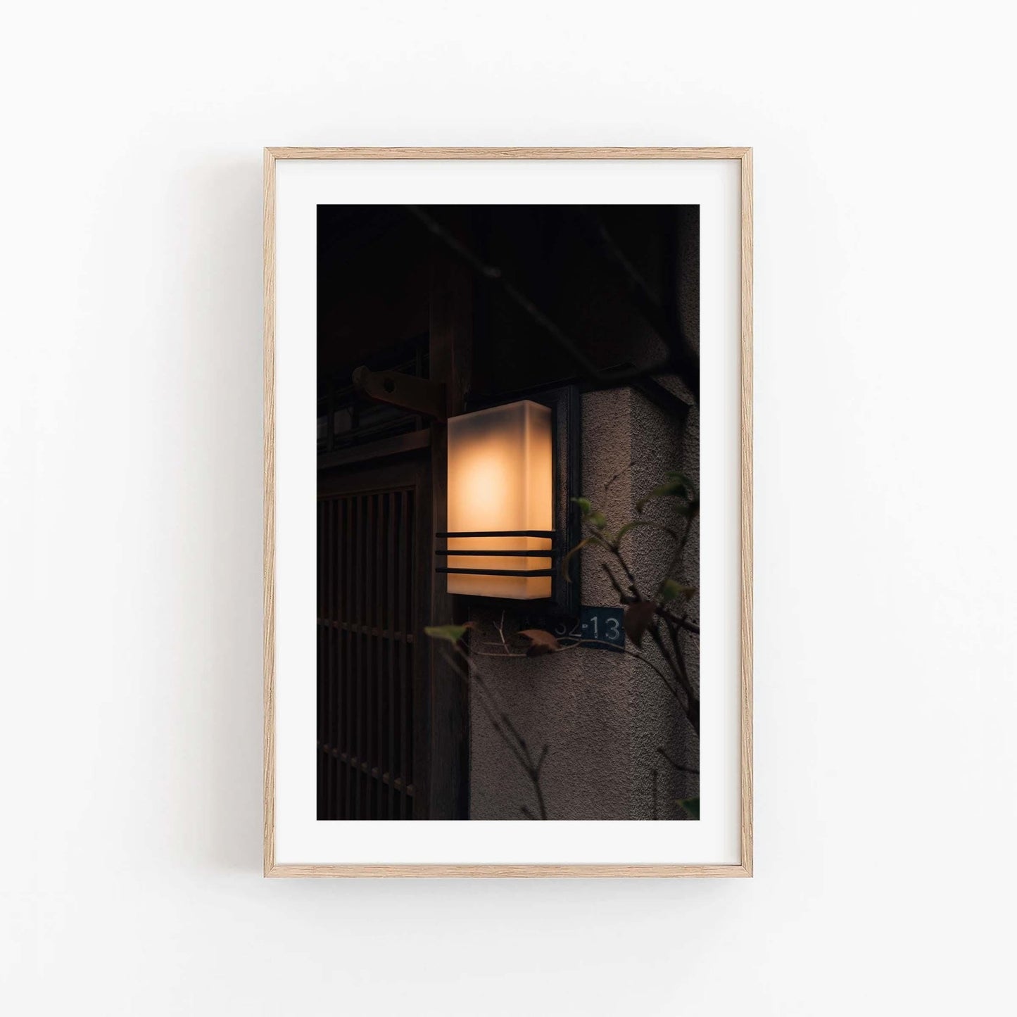 Framed photo titled Zen Ambience, featuring an illuminated wall lamp on a building with a house number plate.