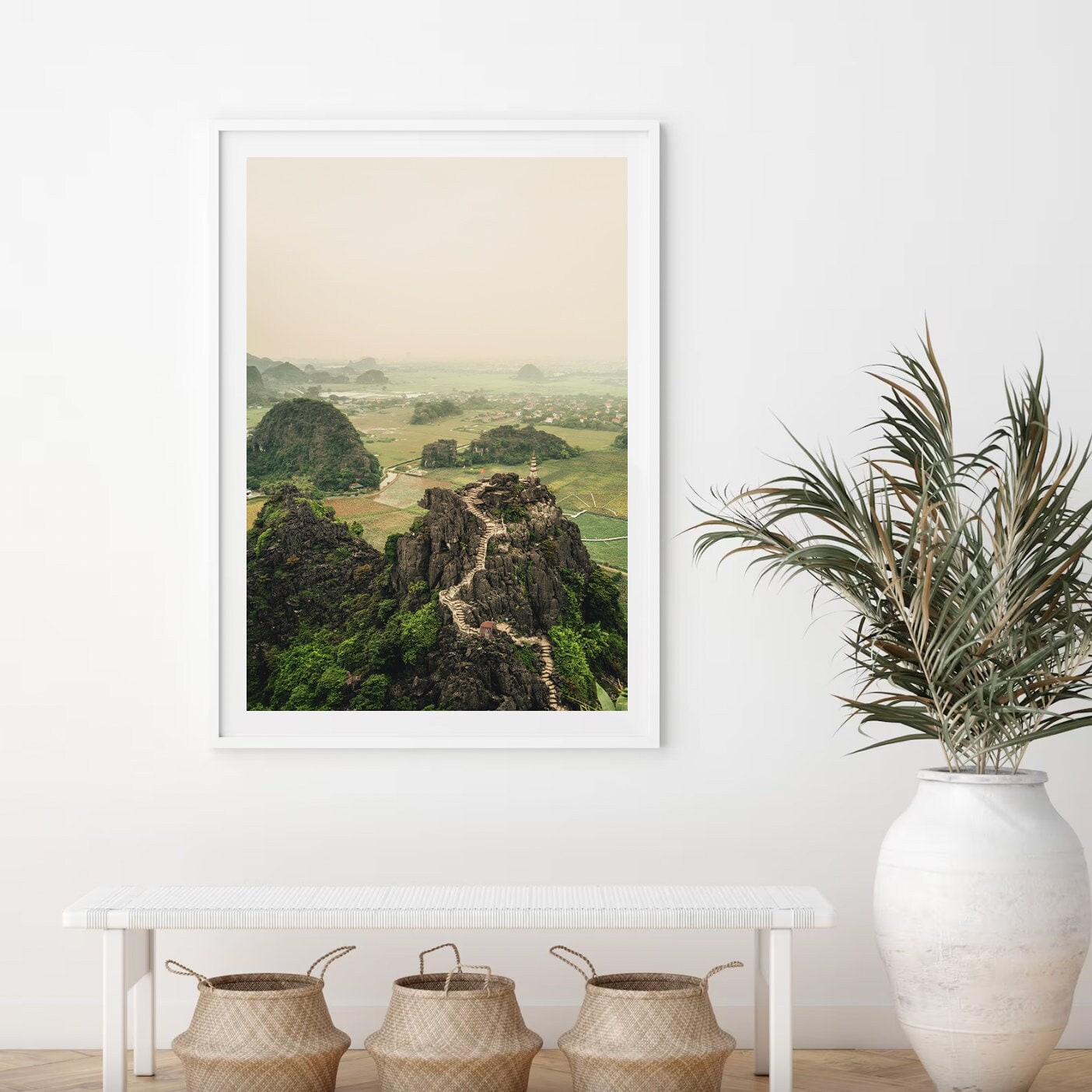 Hang Mua Peak I photo on a white wall above a bench, next to a plant and three woven baskets.